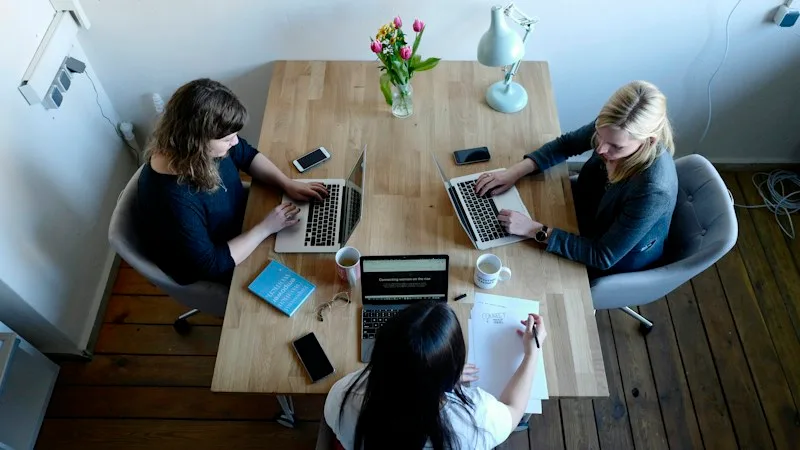 Three coworkers sharing files on laptops around a table