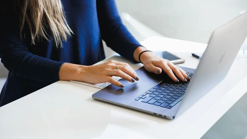 Person typing on a laptop at a white desk to manage business email