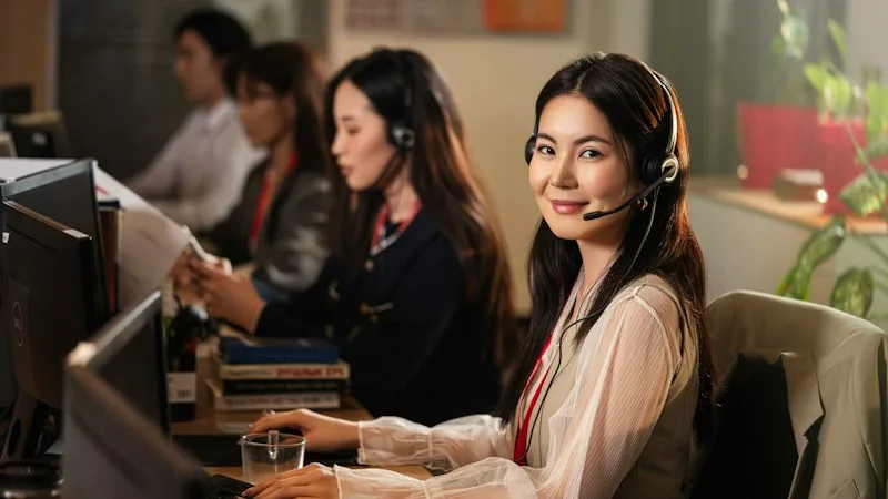 Smiling help desk technician wearing a headset at a computer