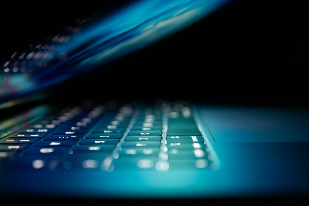 Close-up of a laptop keyboard glowing blue in the dark