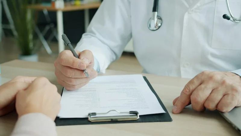 Physician signing a document on a clipboard during a patient visit